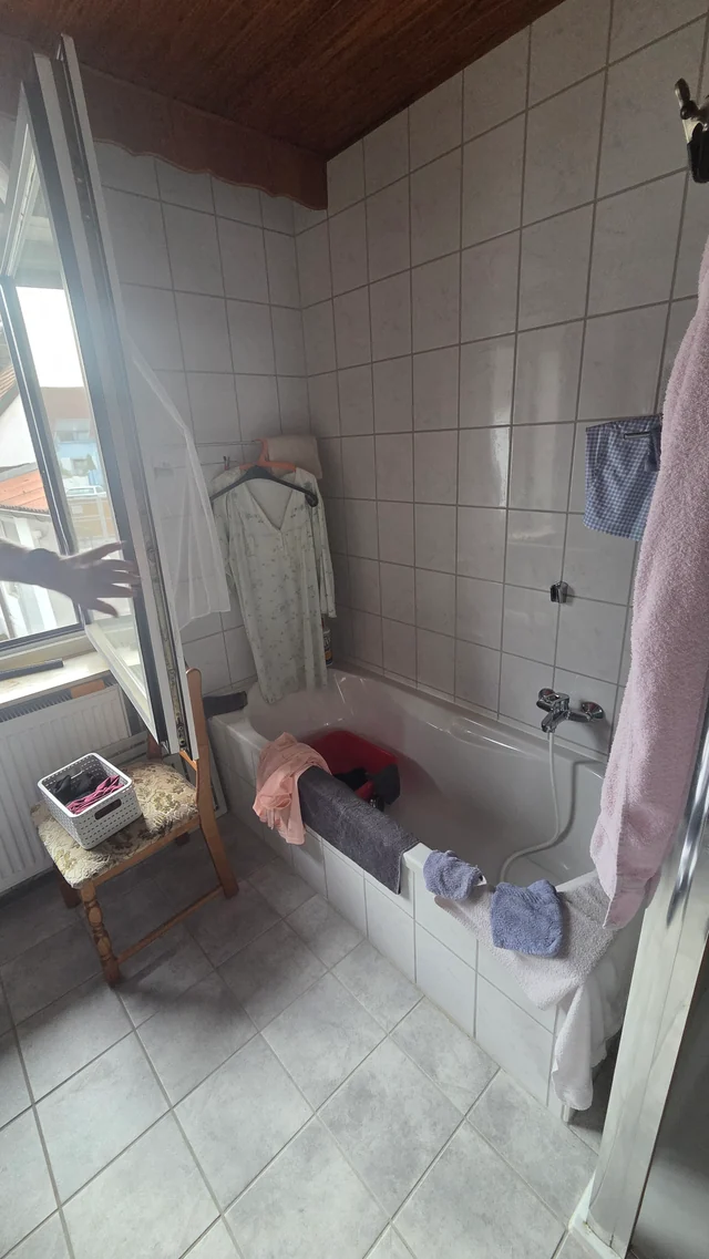 Bestehendes Bad mit Badewanne, gefliesten Wänden und hohem Wanneneinstieg